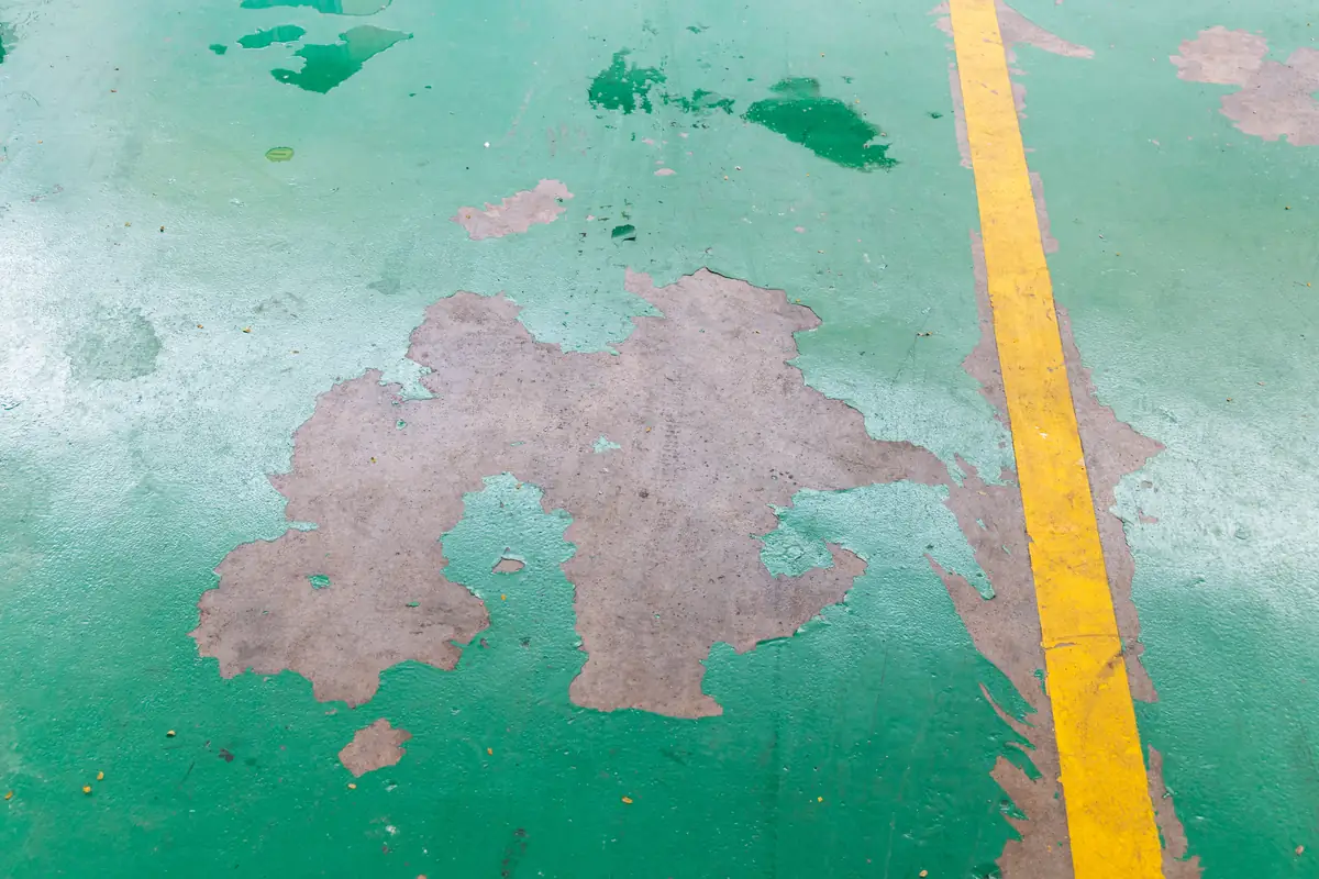 Green commercial floor coating peeled away from a smooth, unground concrete slab